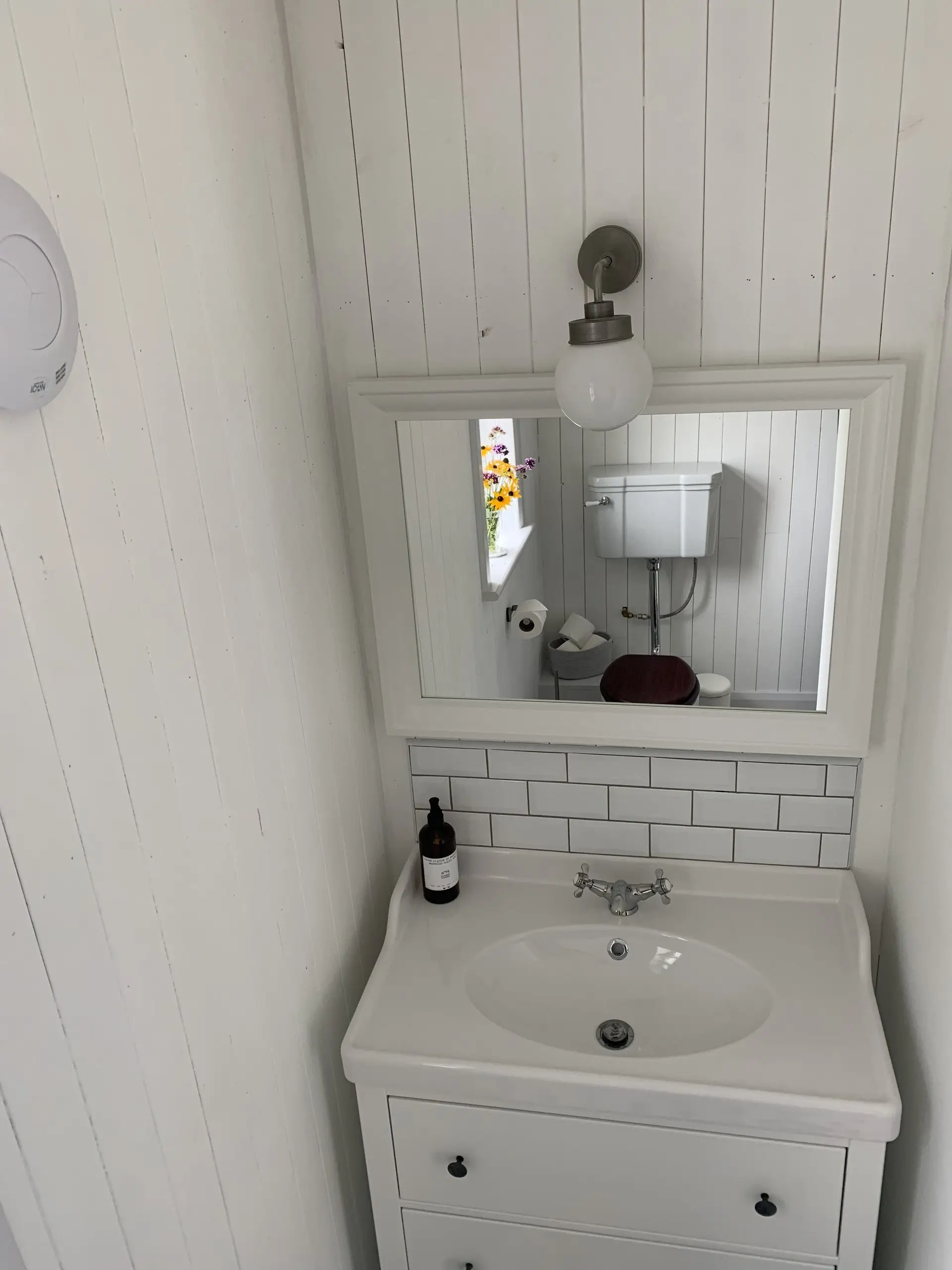 A bathroom sink and mirror with fresh flowers on the sill and white metro tiling.