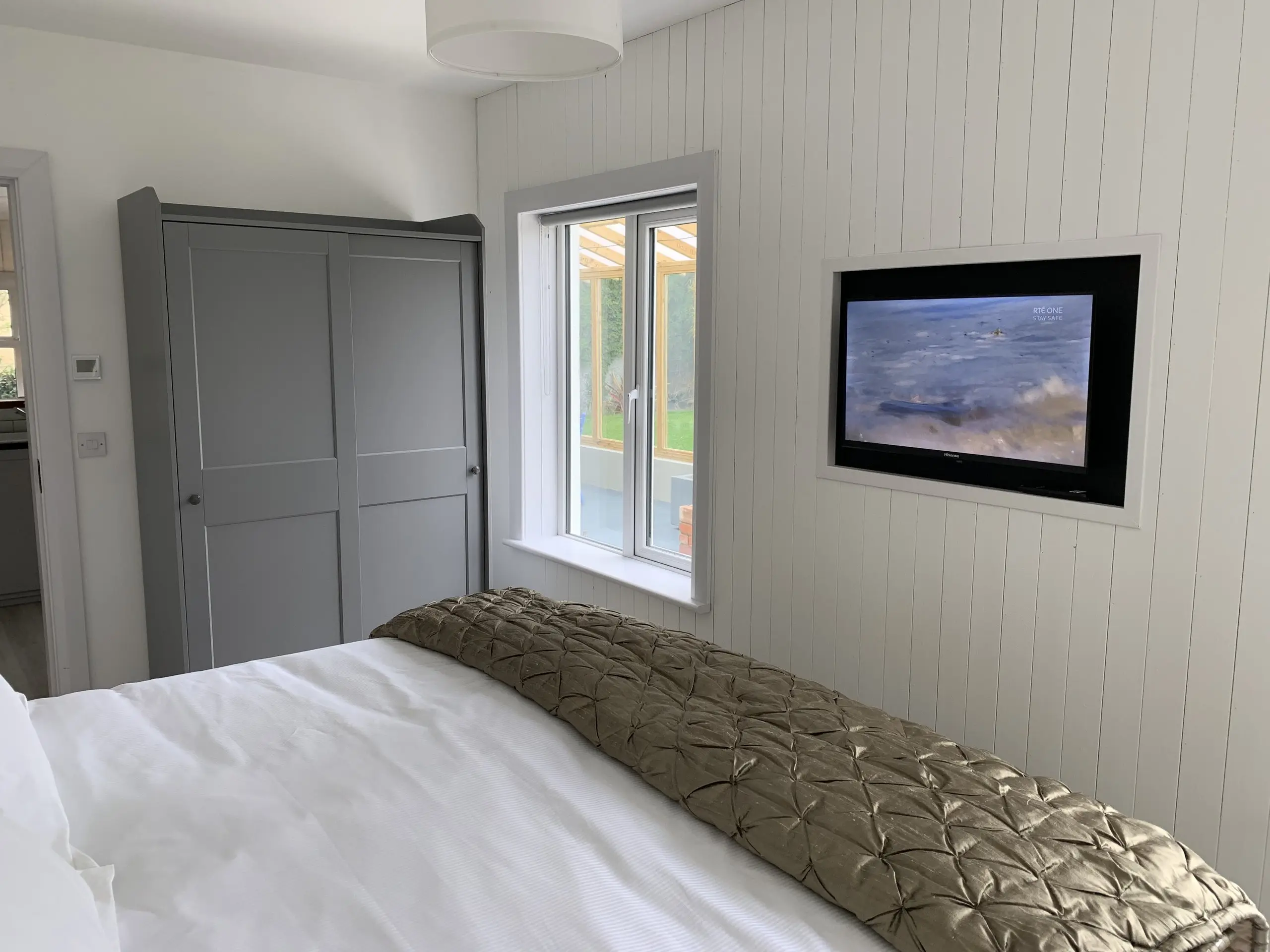 The Garden Bedroom seen from the side, bed made up in white and olive, with a framed picture on the panelled wall.