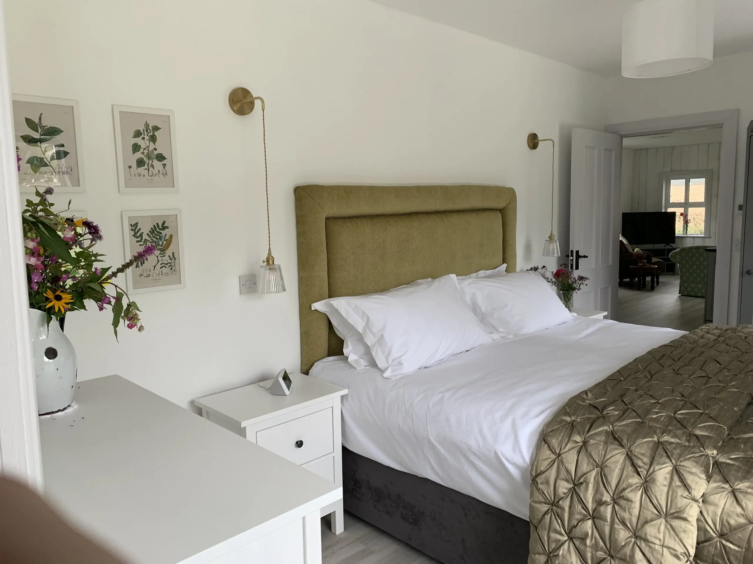 The Garden Bedroom with a vase of garden flowers on the bedside table, olive headboard and botanical prints on the wall.