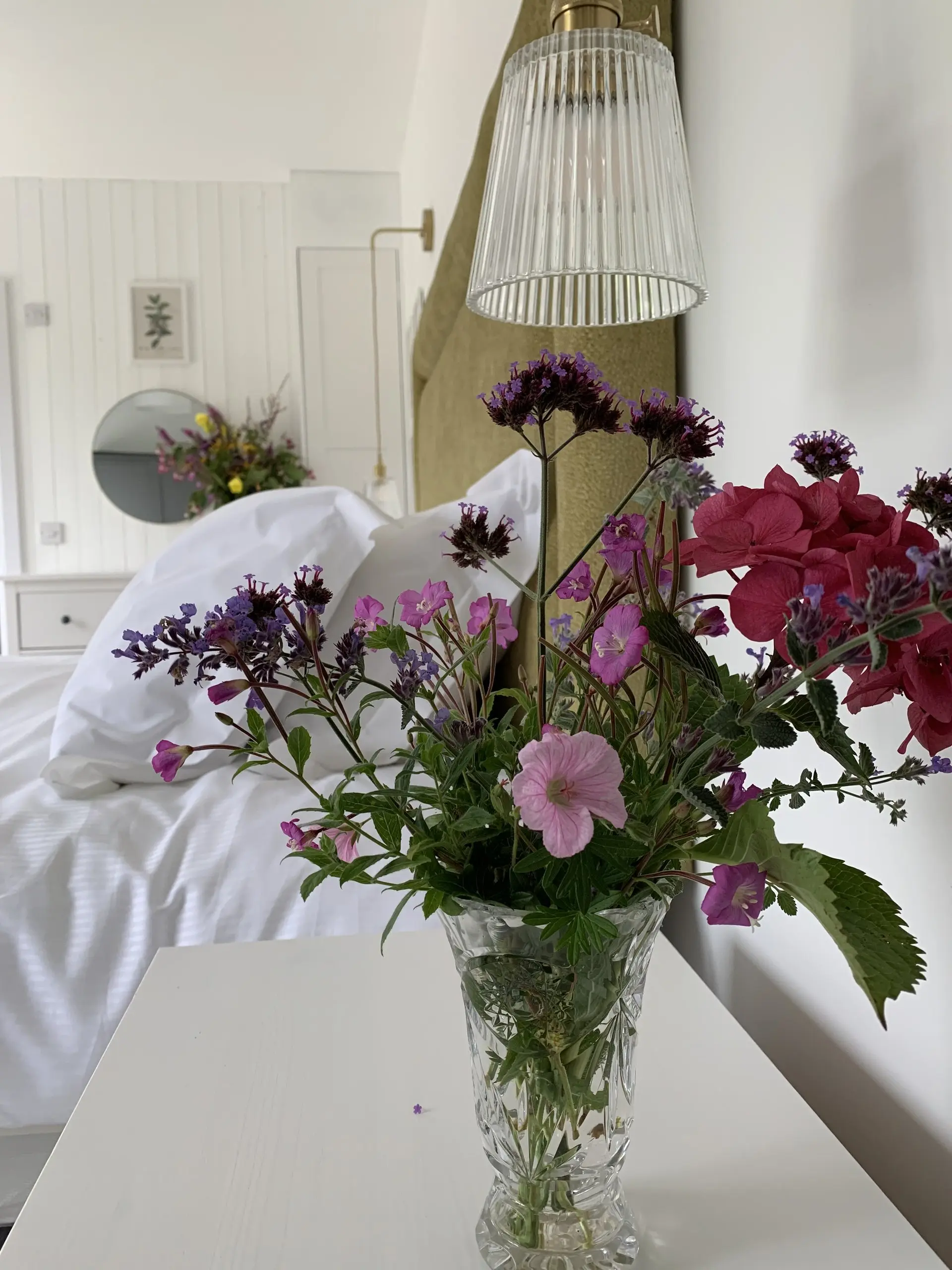 A vase of pink and purple garden flowers on the bed, close up, against crisp white linen.