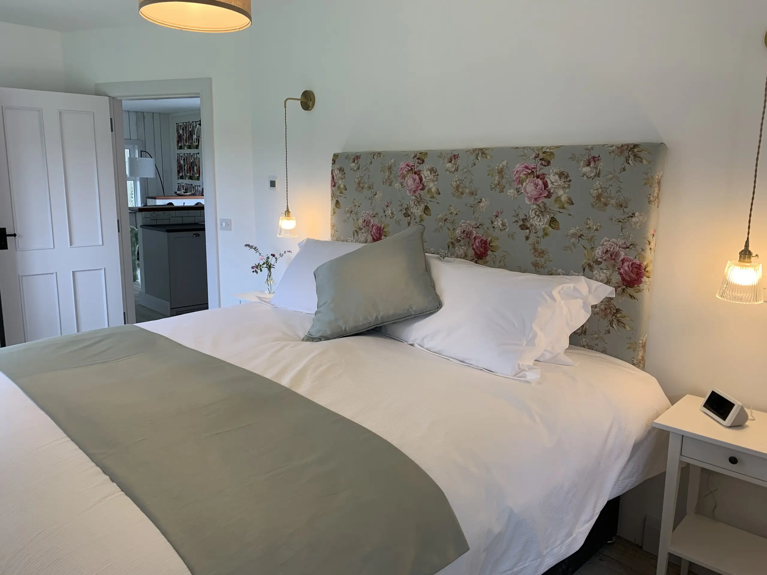The Paddock Bedroom with the floral headboard and sage green throw, a pendant light and doorway through to the ensuite.