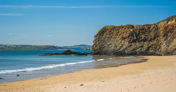 Dollar Bay: a sheltered sandy cove enclosed by green headlands and clear blue water.