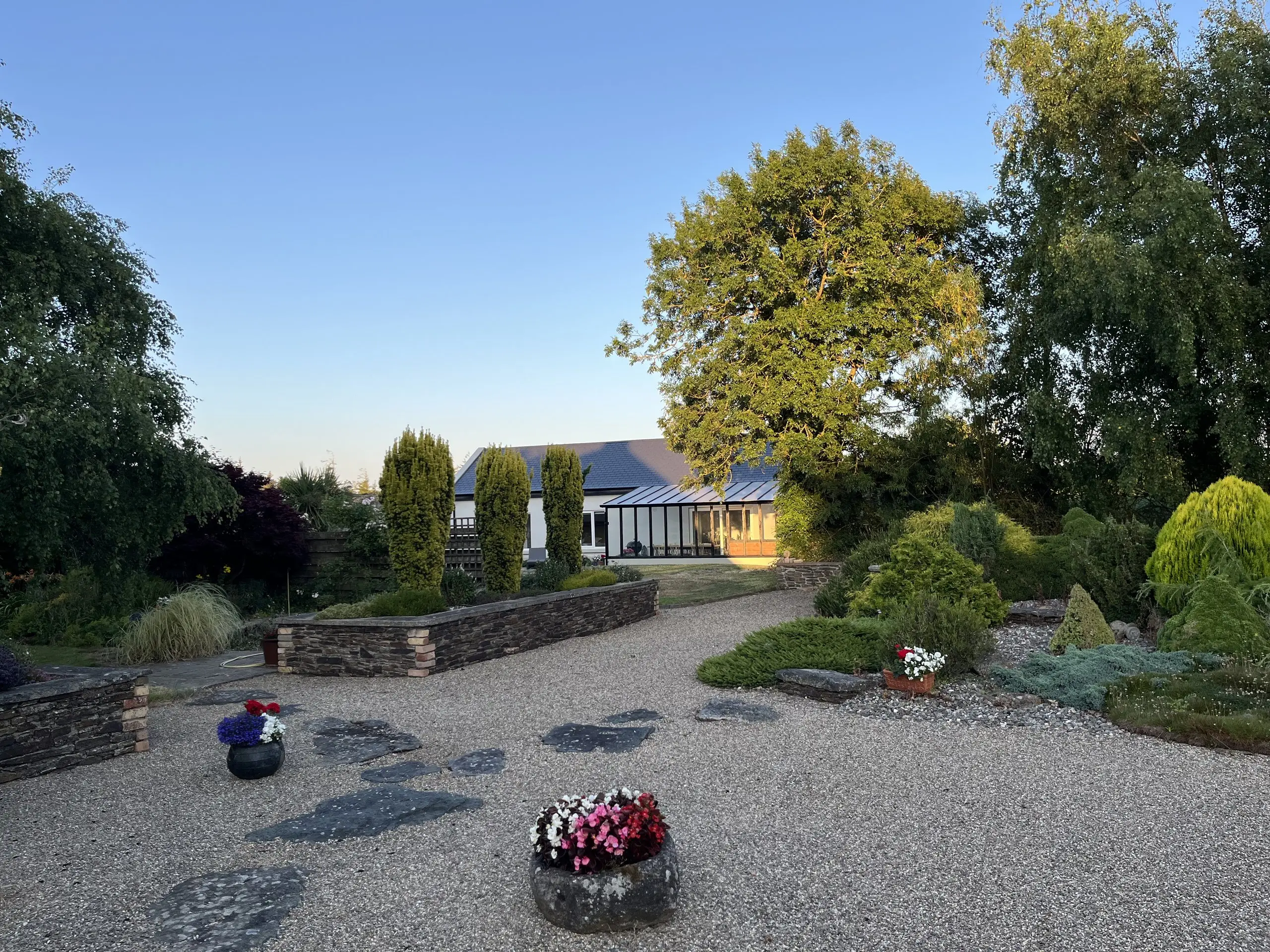 The cottage and garden at golden hour, seen from across the lawn with the planted borders in the foreground.