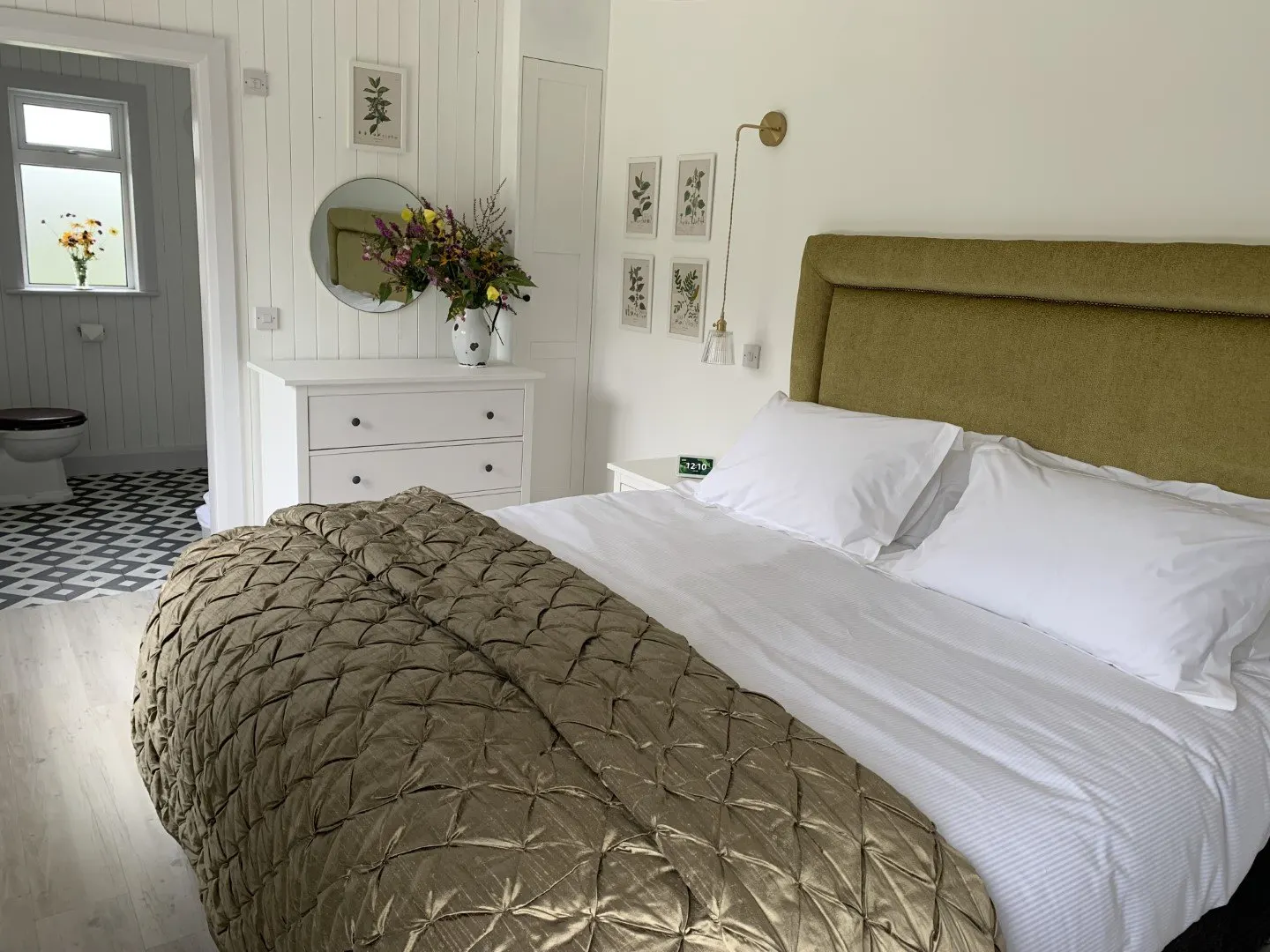 The garden bedroom: a super-king bed with a quilted olive throw, white panelled walls and a dressing table.