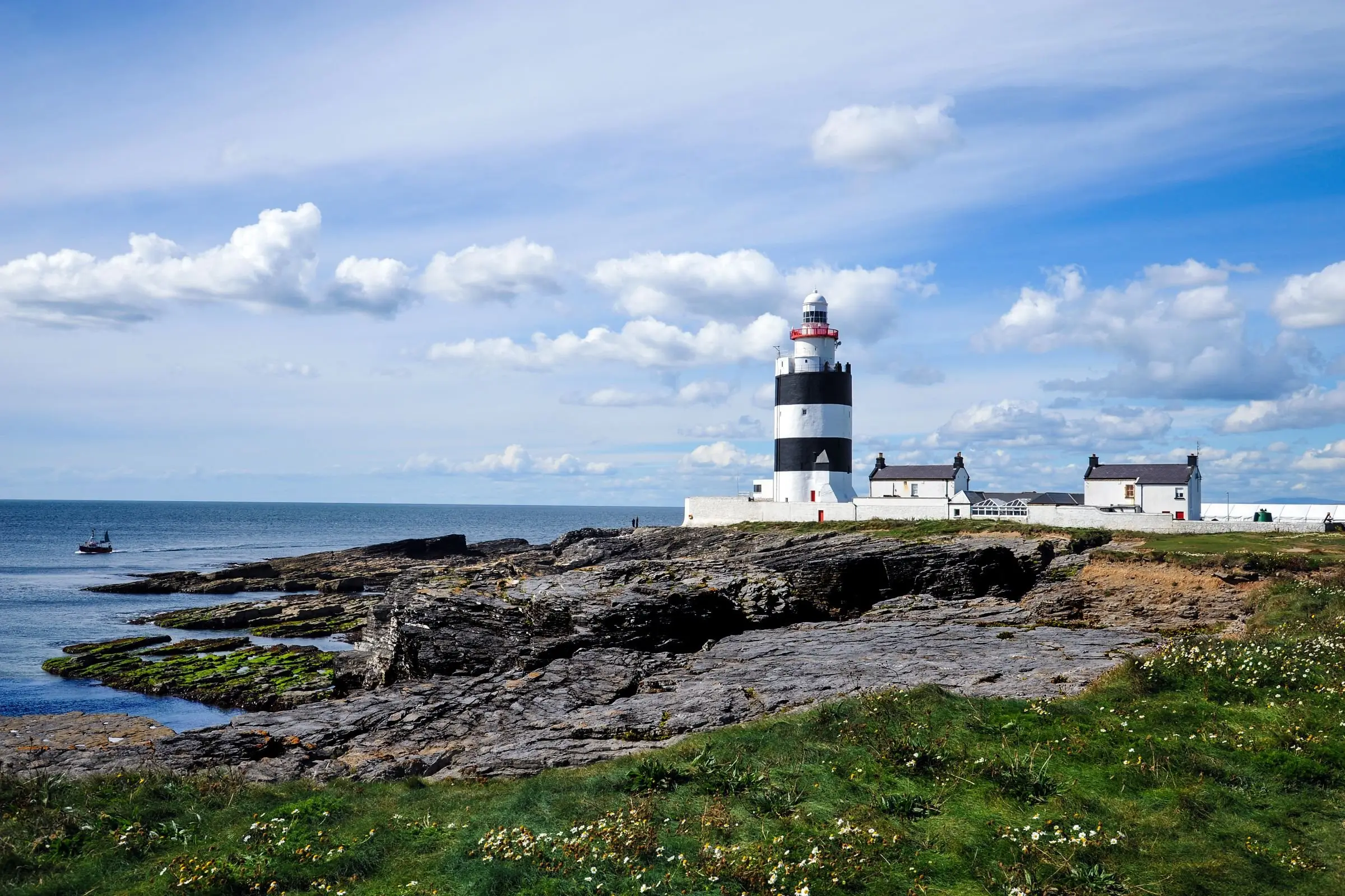 Hook Head lighthouse standing above waves breaking on the rocks at the tip of the peninsula.