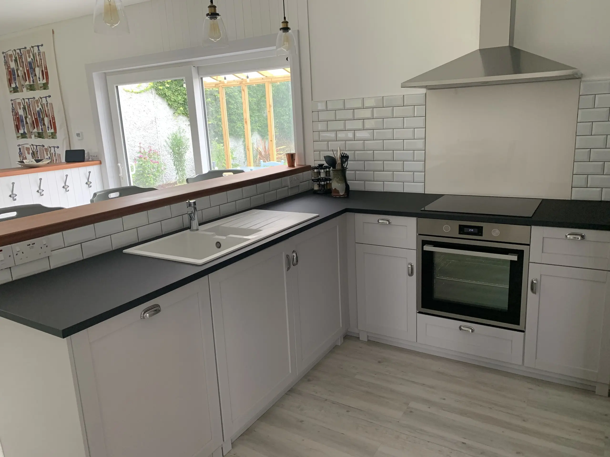 The run of kitchen units with the sink under the window and the oven beside it, dark worktops throughout.