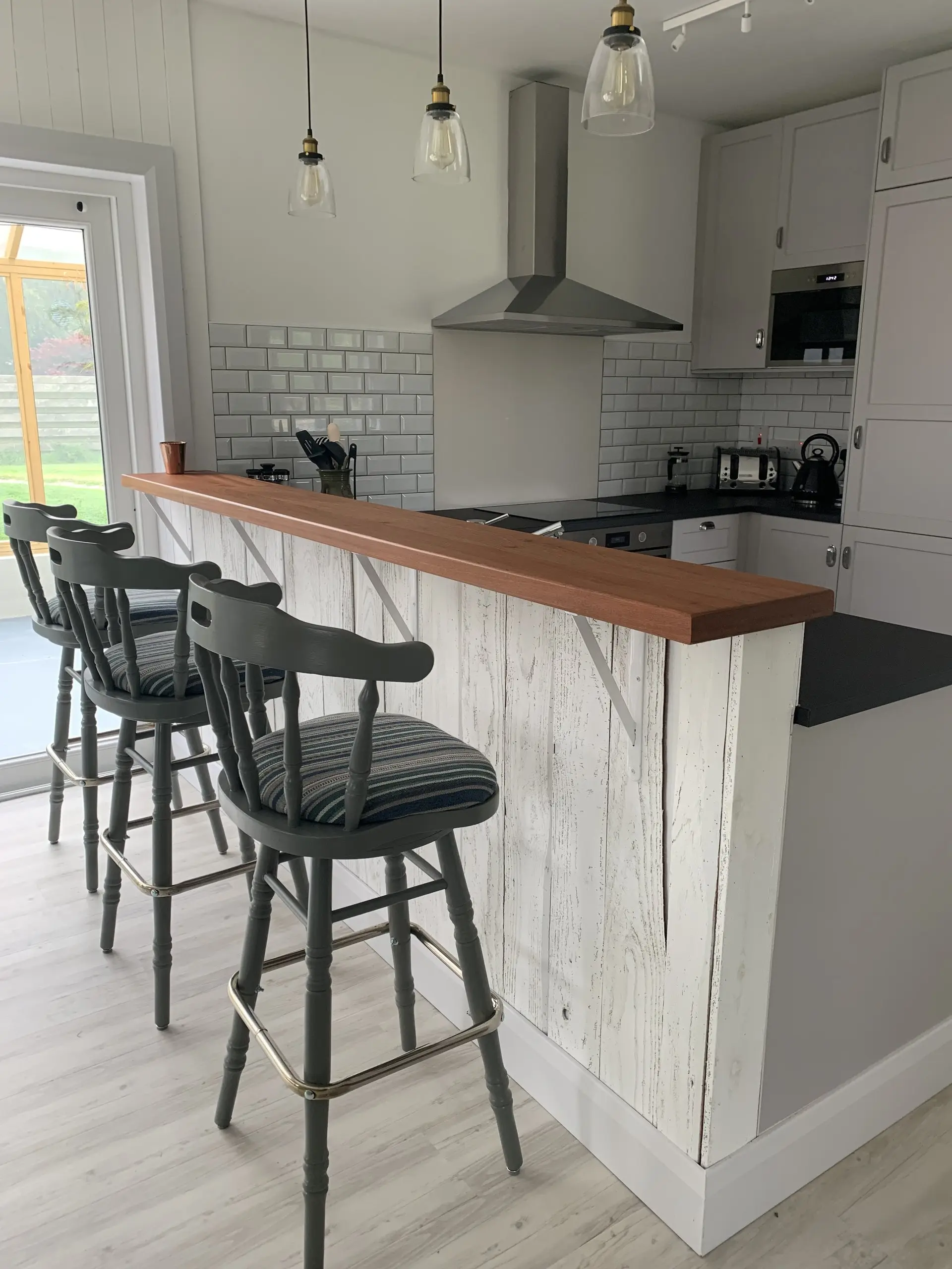 The wooden breakfast bar with two stools drawn up, looking into the kitchen.