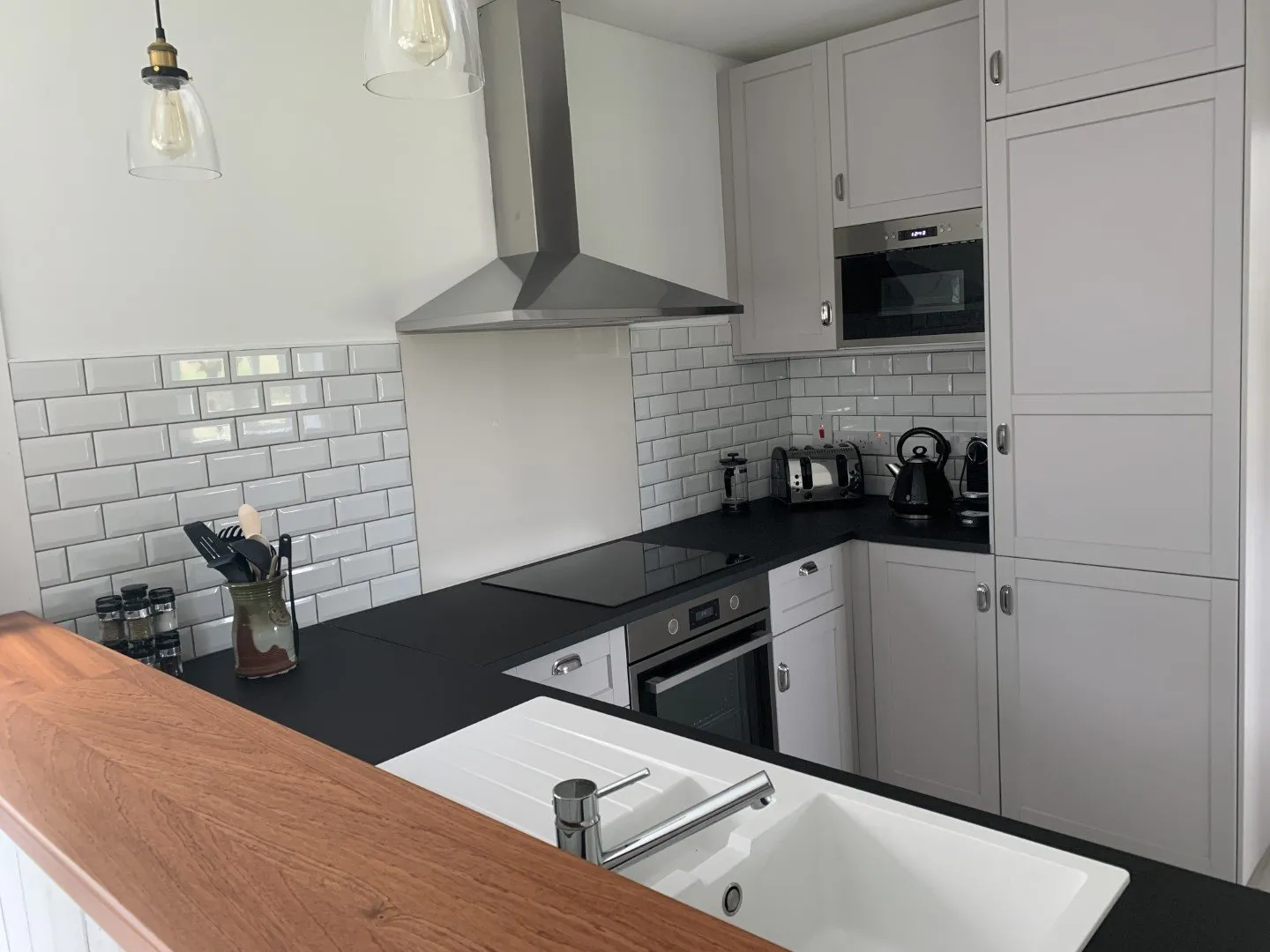 The kitchen: white metro-tiled walls, dark worktops, an integrated oven and hob, and a wooden breakfast bar.