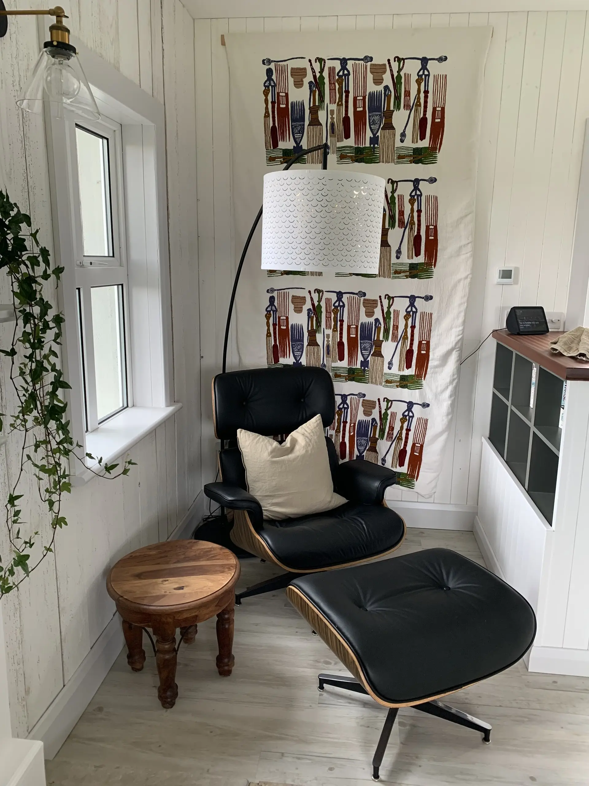 The reading nook: a black leather lounge chair and footstool by a window, with a wall of books and trailing ivy behind.