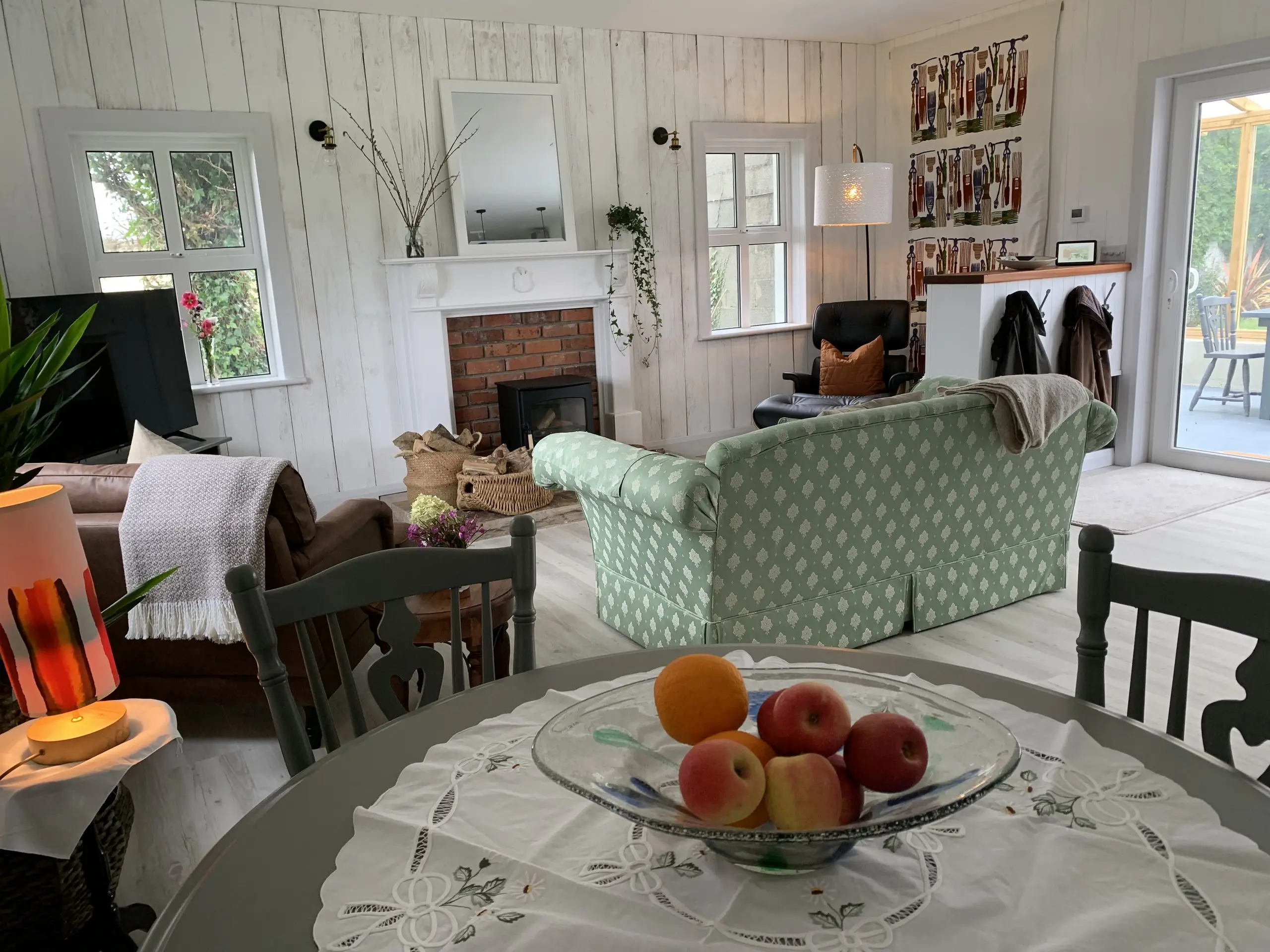 The open-plan living and dining area with the sofa, dining table and brick fireplace, doors opening onto the garden.