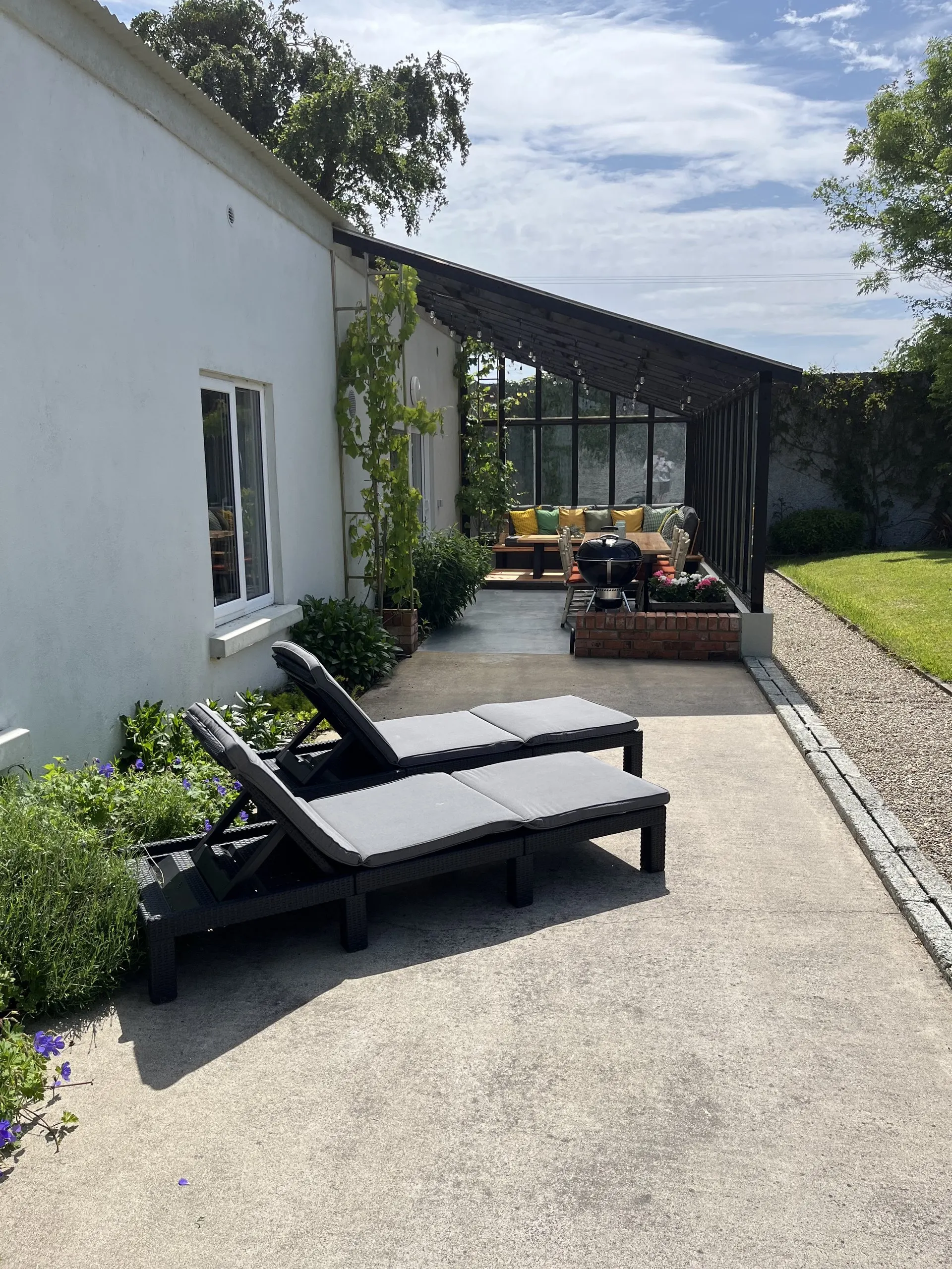 Two sun loungers with towels on the terrace outside the cottage, beside planting and a barbecue.