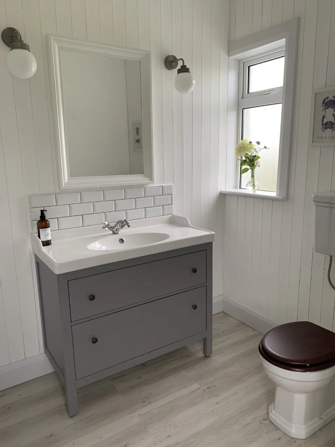 A cottage bathroom with white panelled walls, a large mirror and an extra-wide grey vanity unit with a basin.