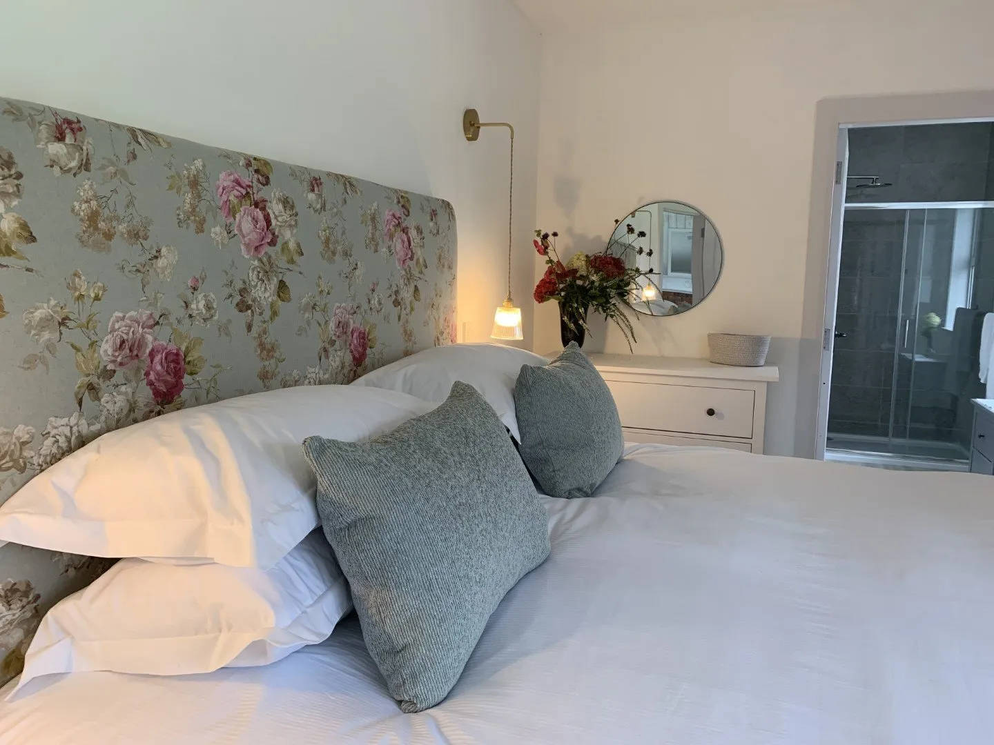 The Paddock Bedroom: a super-king bed with white linen and blue cushions, a floral upholstered headboard and a bedside lamp.