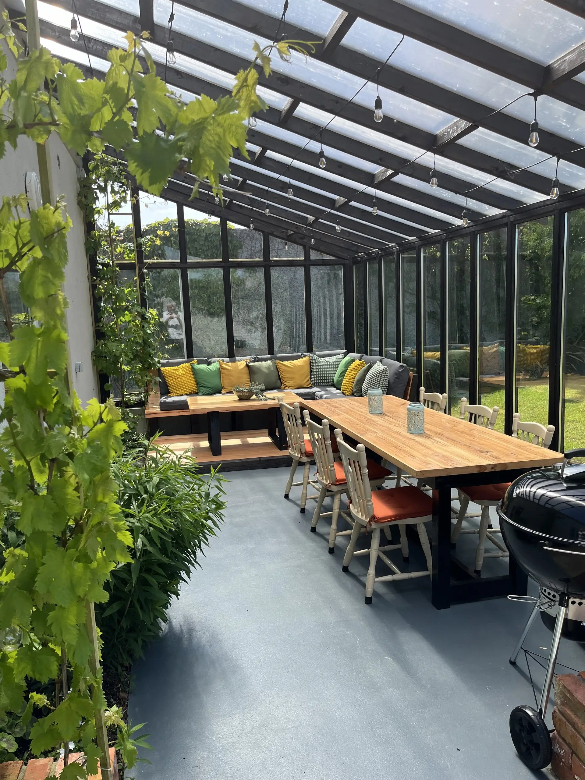 The glazed porch with its corner bench, dining table and scatter cushions, the garden visible through the glass on every side.