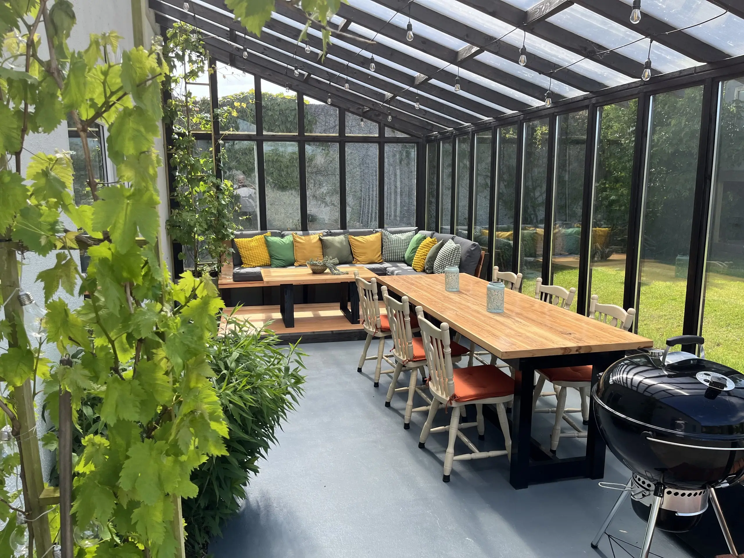 The porch and terrace, the vine trained along the glass roof, the dining table and barbecue looking out to the lawn.
